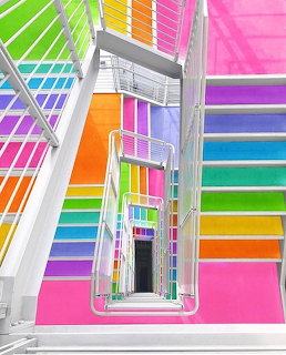 Top-down view of a colorful rainbow-painted stairwell with white metal railings