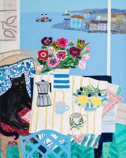 Painting of a black cat on a blue chair near anemones in a vase with a seaside village visible through a window