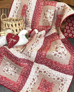 Red and white patchwork quilt with floral patterns draped over wicker chair