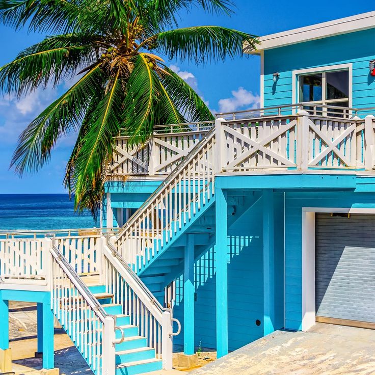 Turquoise beach house with white stairs, palm tree, and ocean backdrop