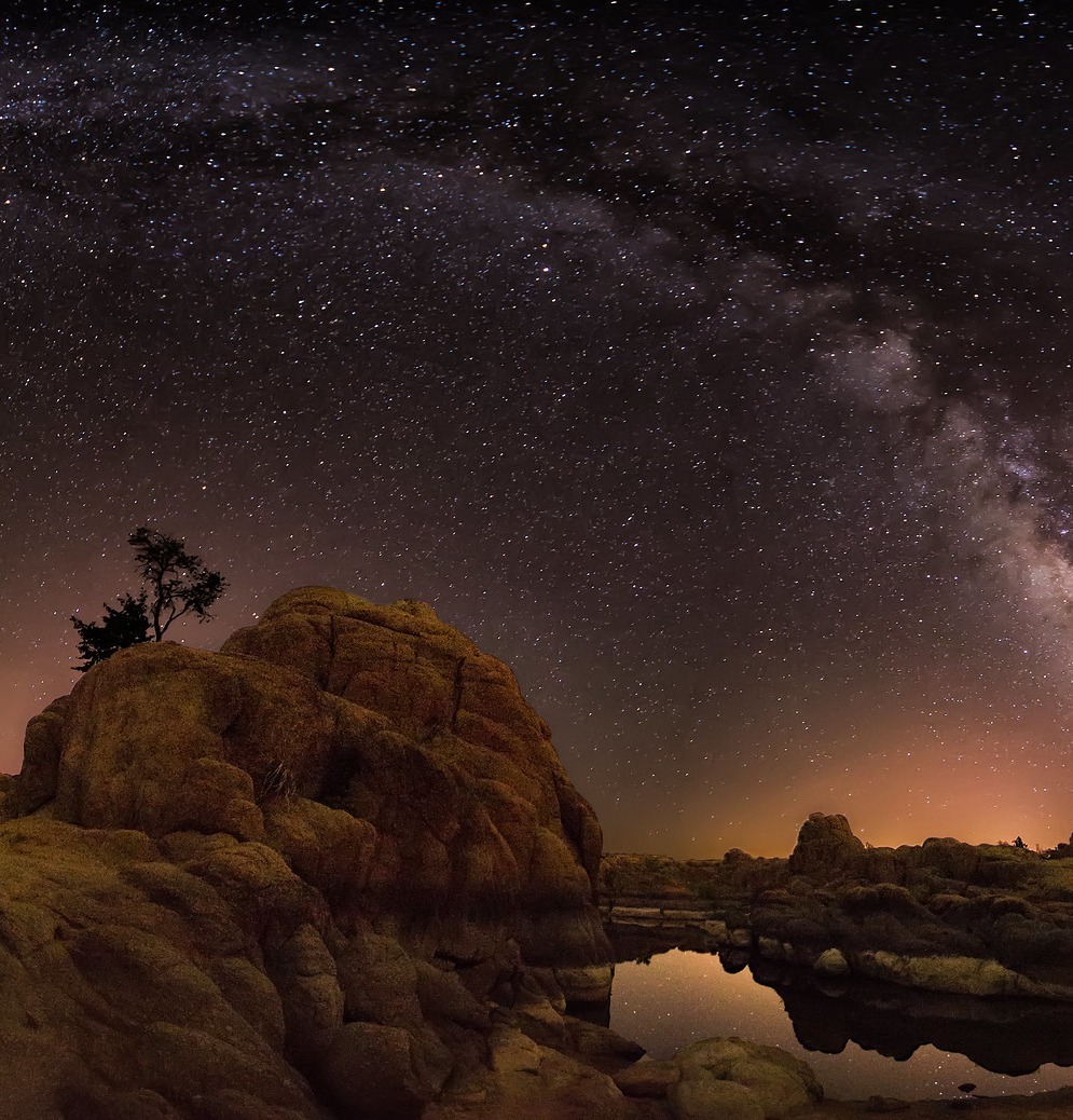 Milky Way galaxy stretching across starry night sky above desert rock formations and small water pool