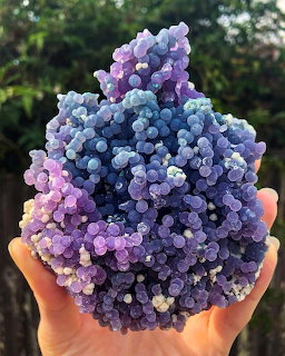 Hand holding purple and blue grape agate crystal with bubble-like spherical formations