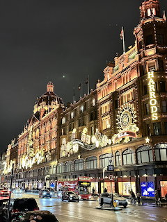 Harrods department store in London lit up with golden lights at night with wet streets