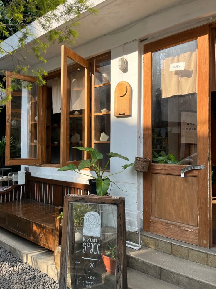 Cozy cafe exterior with wooden doors, glass windows, bench, and a chalkboard sign surrounded by plants