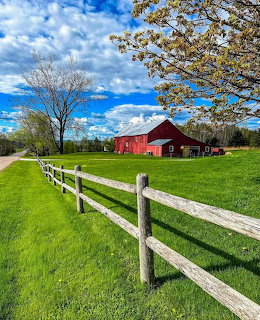 Red barn with white fence in green spring field under blue sky with clouds