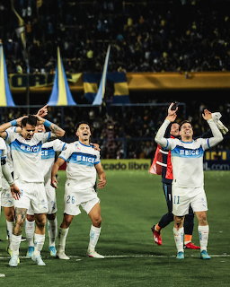 Soccer team in white jerseys celebrating on field at night with crowd in background