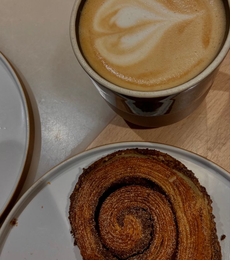 Latte with foam art next to a cinnamon roll on wooden surface