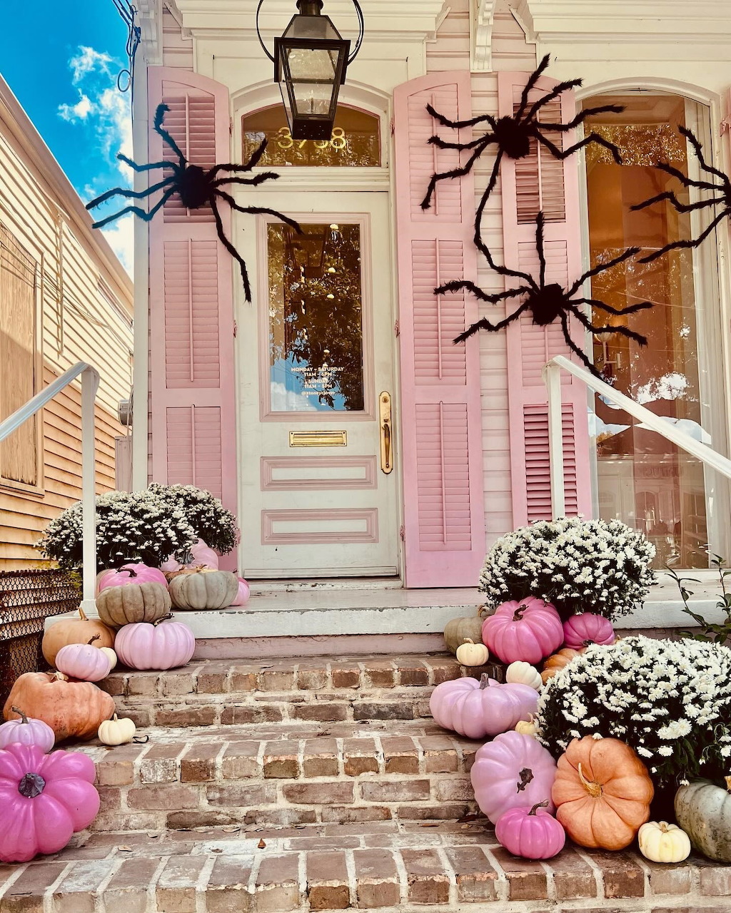 Pink house entrance with pastel pumpkins, black spider decorations, and fall flowers for Halloween
