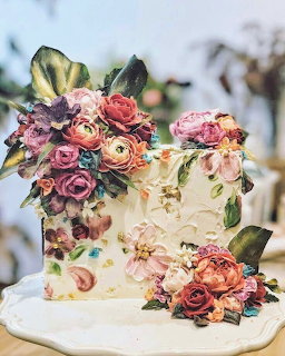 White floral cake decorated with pastel roses and blossoms on a cake stand
