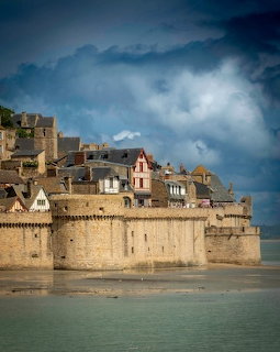 Le Mont Saint Michel stone walls and historic buildings beside tidal water under dark clouds