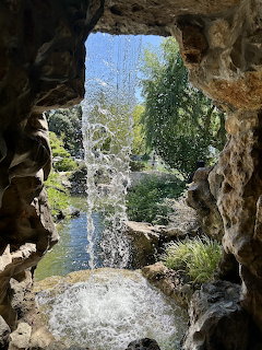 View through rock cave opening to Japanese garden with waterfall and pond