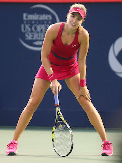Female tennis player in pink outfit crouching in ready position holding a racket on a hard court