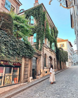 Person walking on cobblestone street past ivy-covered building with turquoise shutters in Lausanne, Switzerland
