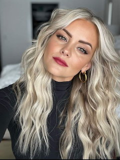 Portrait of woman with platinum blonde wavy hair, pink lipstick, and gold hoop earrings in black turtleneck