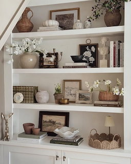 White built-in bookshelf decorated with vases, books, framed pictures, baskets, and white flowers