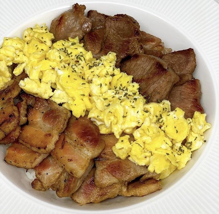 White plate with grilled meat strips and scrambled eggs garnished with black pepper