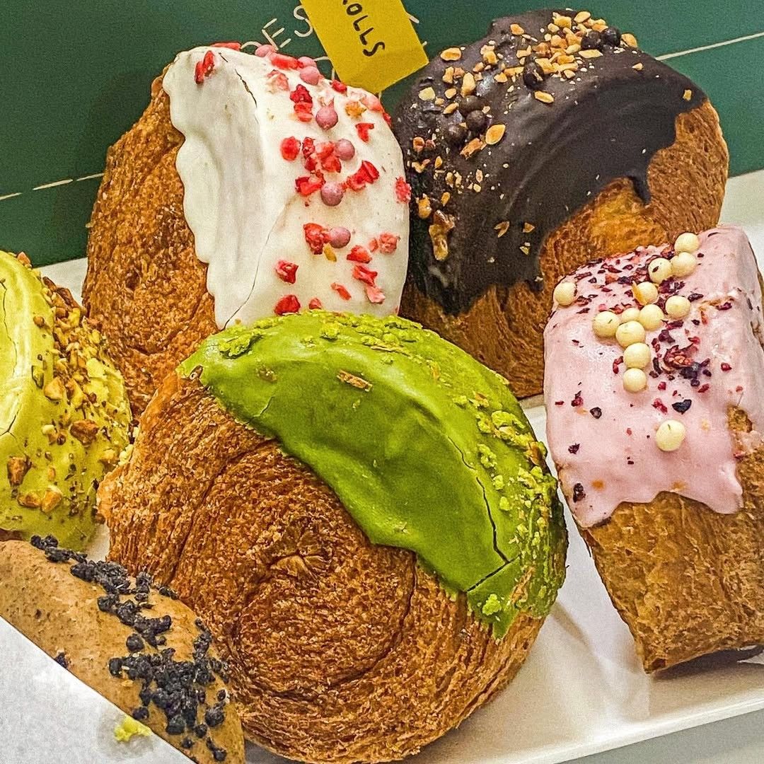 Croissants decorated with colorful icing including chocolate, green matcha, pink, and white glazes with sprinkles