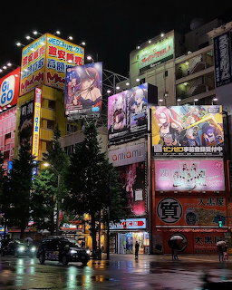 Night city street with illuminated anime billboards on buildings and wet pavement