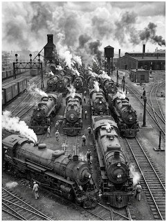 Black and white photo of steam locomotives in a busy railroad yard with smoke