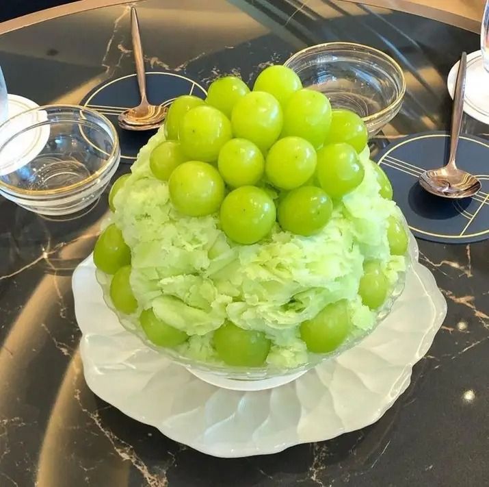 Green shaved ice mound topped with fresh green grapes on white plate