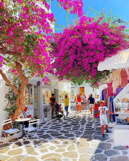 Mykonos street with white buildings, pink bougainvillea, patterned pavement, and tourists browsing shops