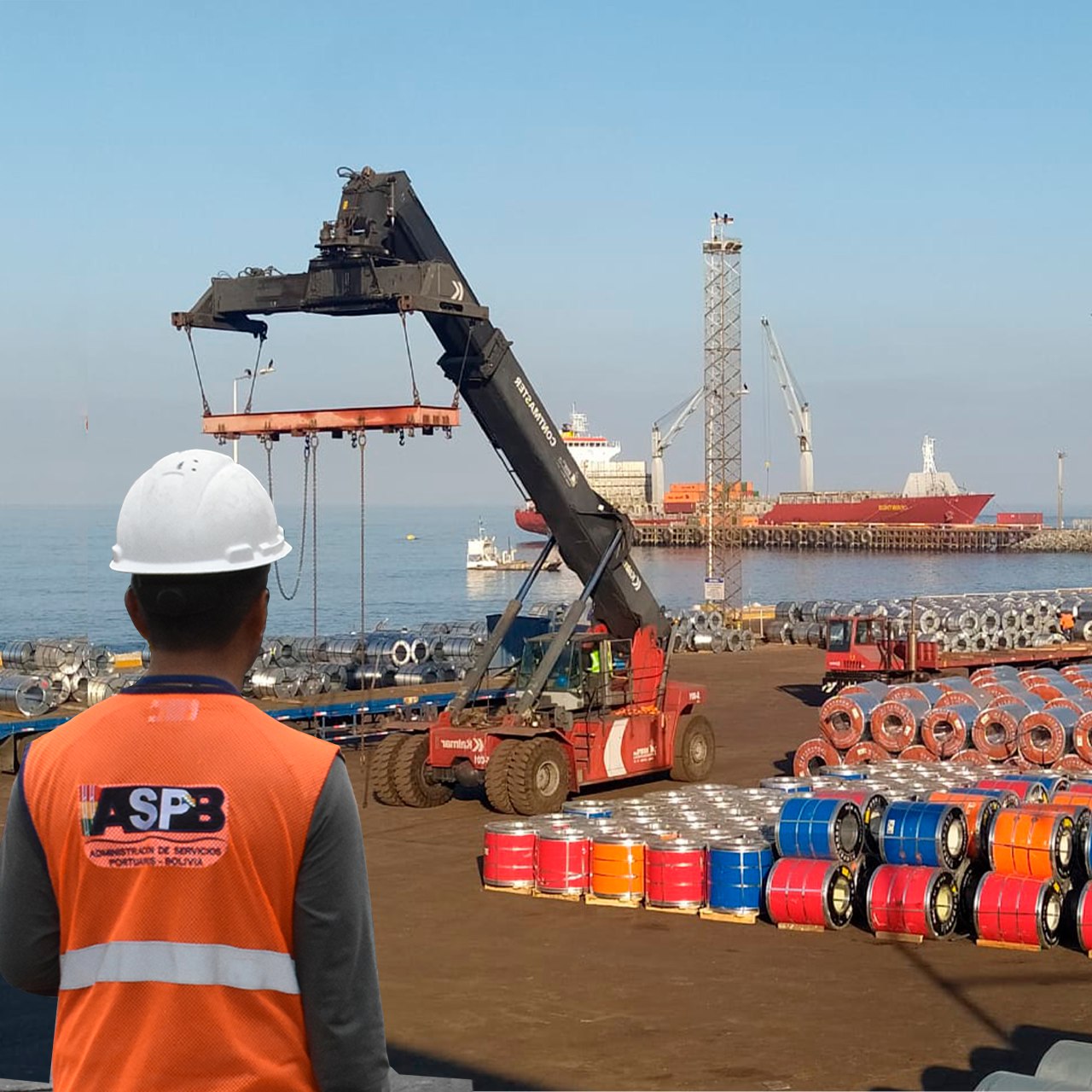 Worker in safety gear watching a crane at an industrial port with ships and colorful barrels