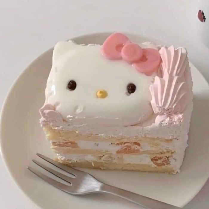 Hello Kitty themed cake slice with white frosting, pink bow, and decorative meringue on white plate with fork