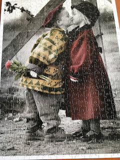 Two children in vintage clothing kiss under umbrella in rain with small dog, selective color emphasizing red dress