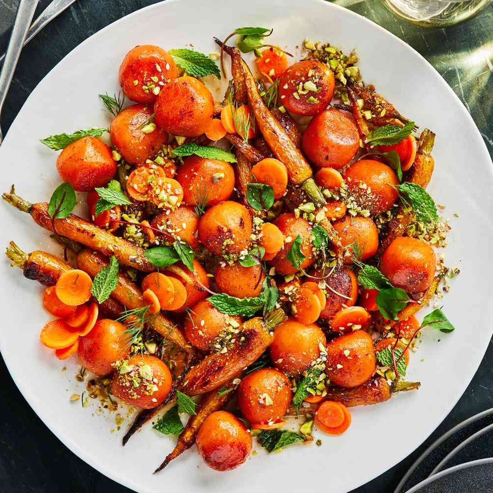 White plate with roasted cherry tomatoes and carrots garnished with fresh mint and crushed nuts