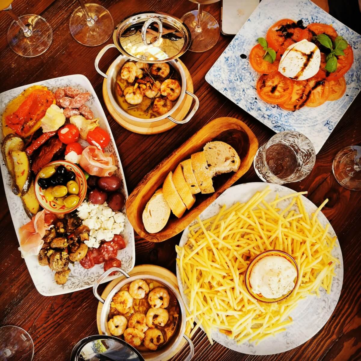 Overhead view of various tapas dishes including shrimp, fries, bread, and antipasto on a wooden table