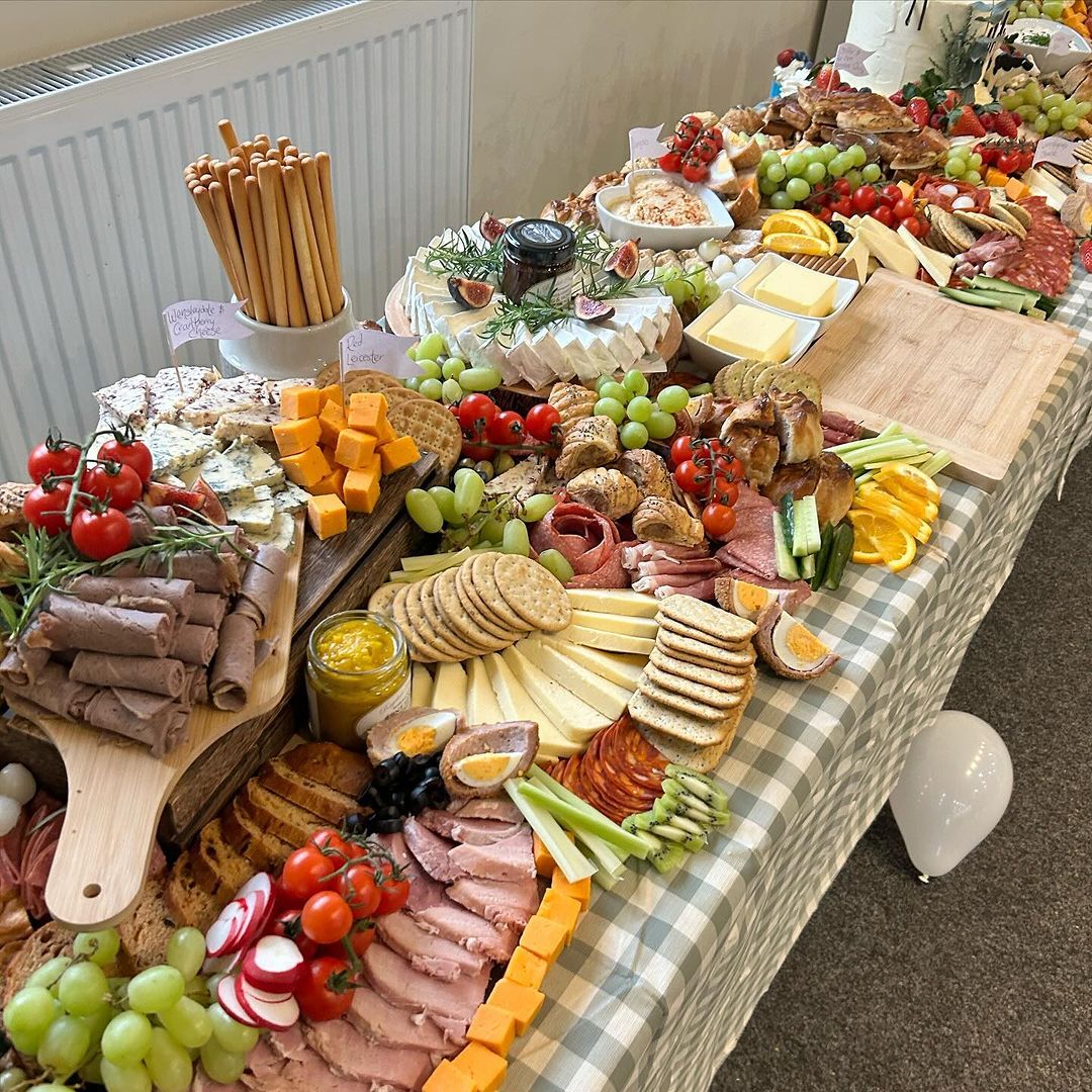 Large charcuterie grazing table with cheese, meats, fruits, and crackers on wooden boards