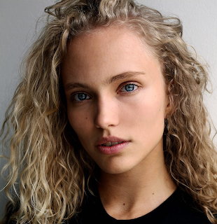 Close-up portrait of a woman with curly blonde hair and blue eyes