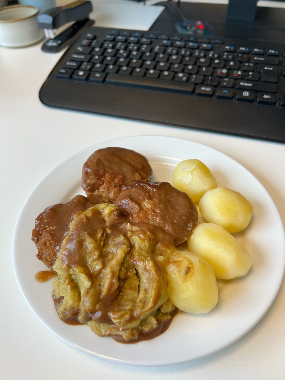 White plate with braised meat in brown gravy and boiled potatoes on a desk