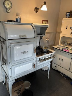 Vintage white stove in an old-fashioned kitchen interior with cabinets, lamp, and wall clock.