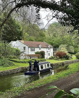 Narrow boat moored on canal beside white cottage with garden and trees