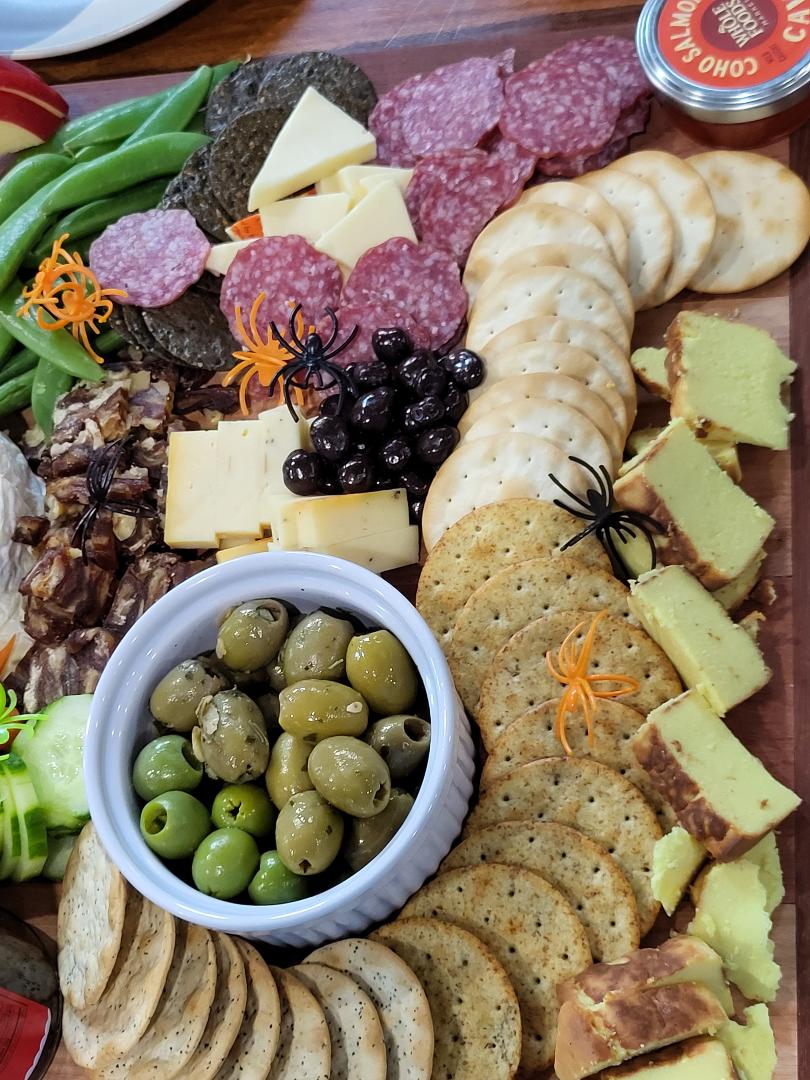 Halloween-themed charcuterie board with cheese, salami, crackers, olives, nuts, and plastic spider decorations