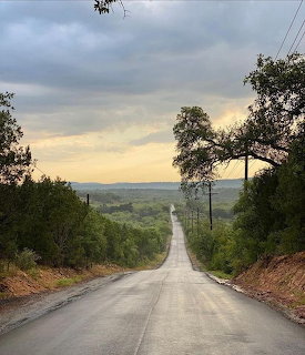 Wet country road leading through green hills under a cloudy sky