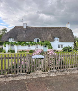 White thatched cottage with wooden fence and garden