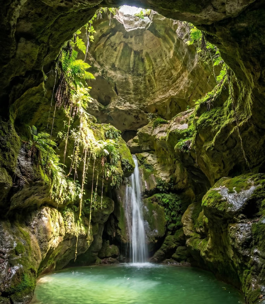 Waterfall inside a mossy cave falling into a turquoise pool