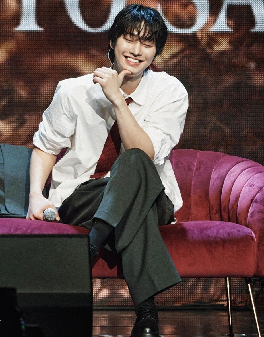 Man in white shirt sitting casually on purple velvet sofa, smiling at camera