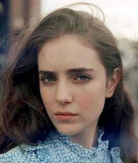 Close-up portrait of a young woman with brown hair, green eyes, and a blue knit sweater