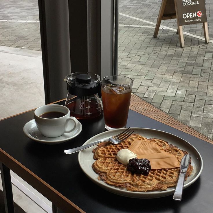 Waffles with butter and syrup served with hot coffee and an iced drink on a cafe table