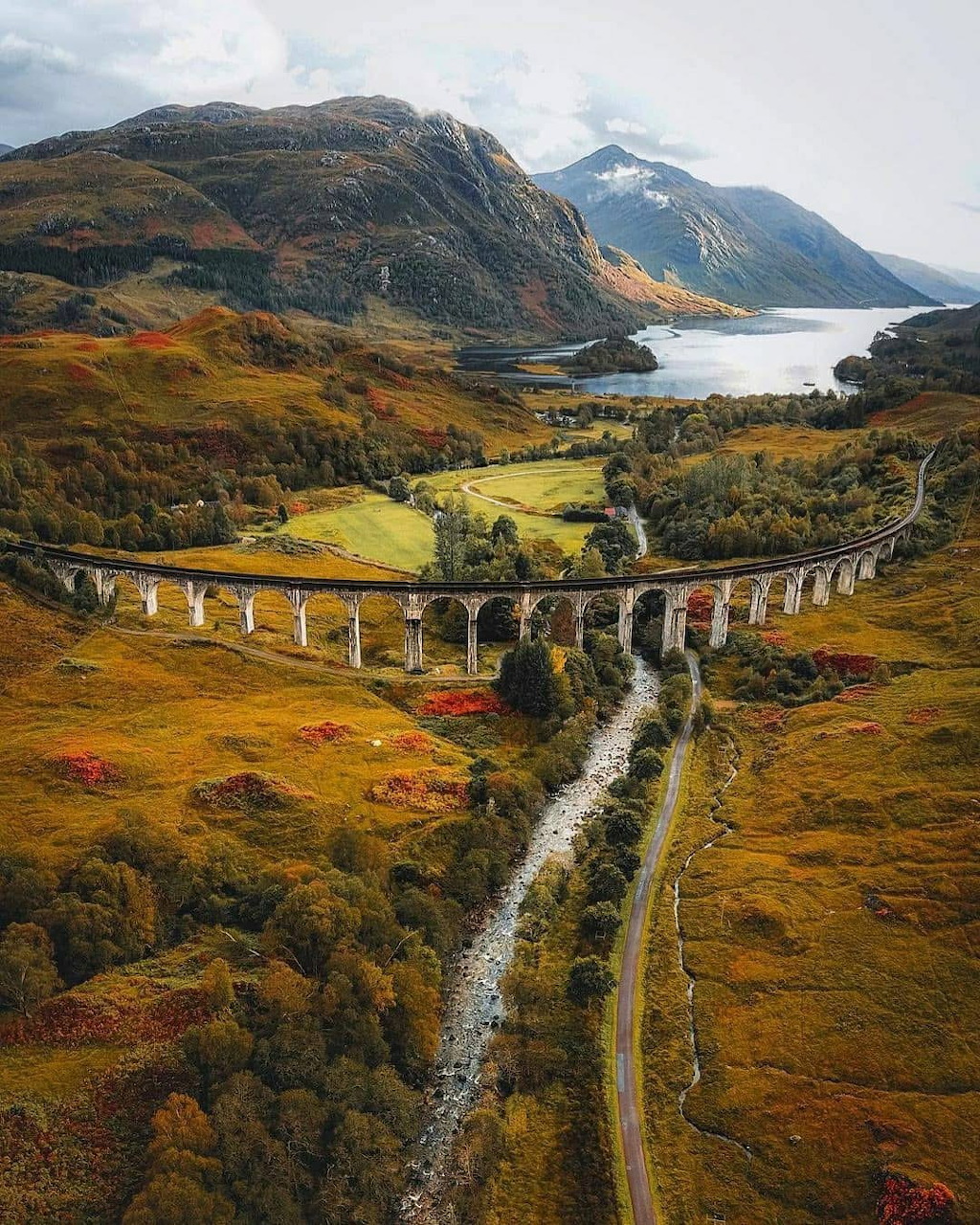 Aerial view of Glenfinnan Viaduct in the Scottish Highlands with autumn hills and a loch in the background
