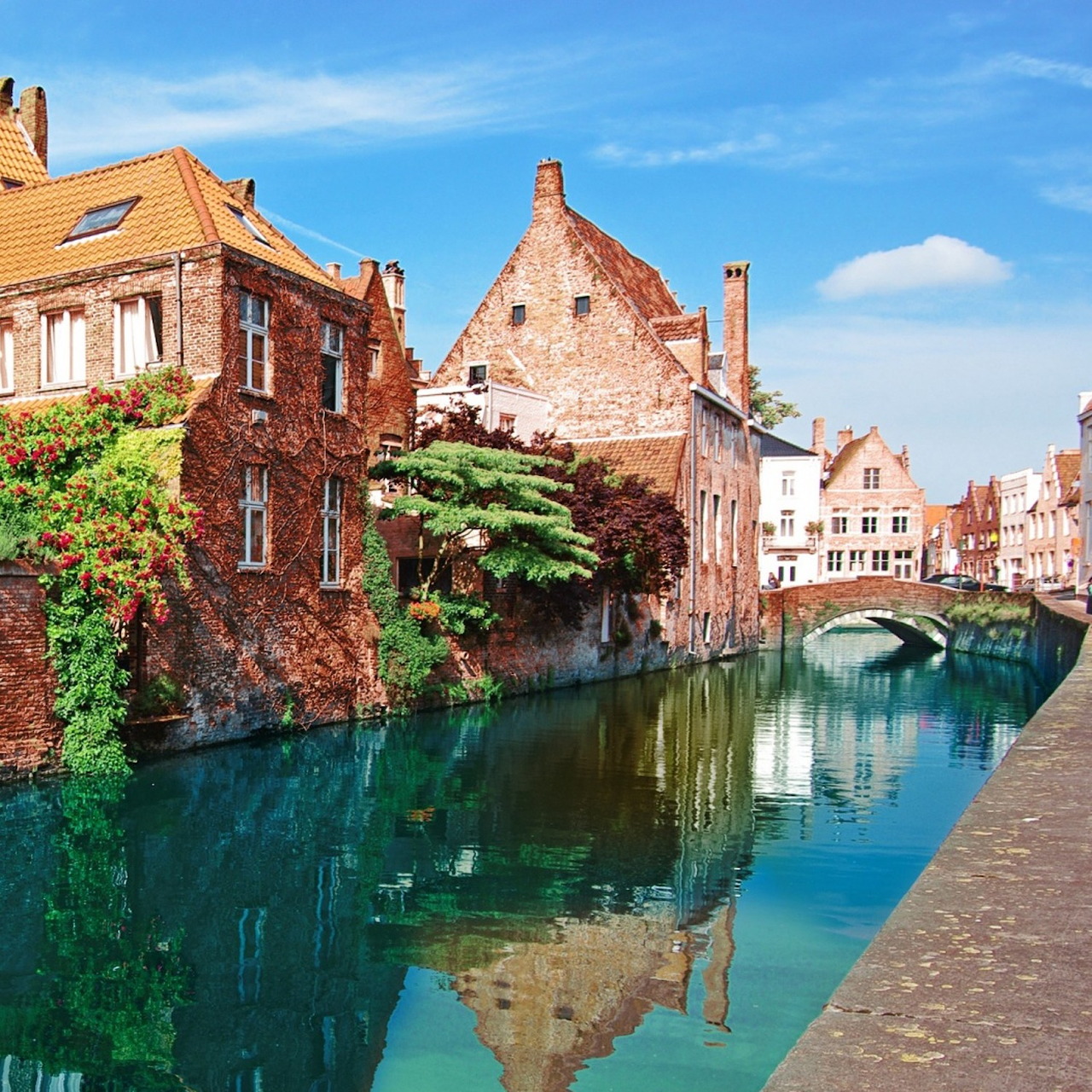 Historic canal with brick buildings, stone bridge, and reflections in turquoise water