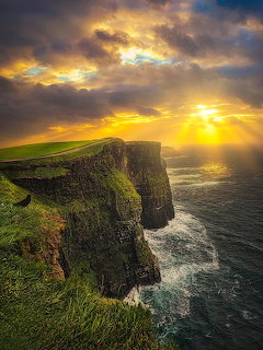 Steep coastal cliffs at sunset with dramatic golden sky and ocean waves below