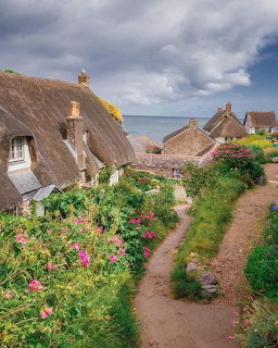 Thatched cottages, flower gardens, and a narrow path overlooking the sea at Cadgwith Cove, Cornwall.