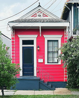 Bright pink tiny house with white trim and blue door on residential street