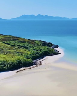 Sandy beach with turquoise sea, green coastal hills, and distant mountains