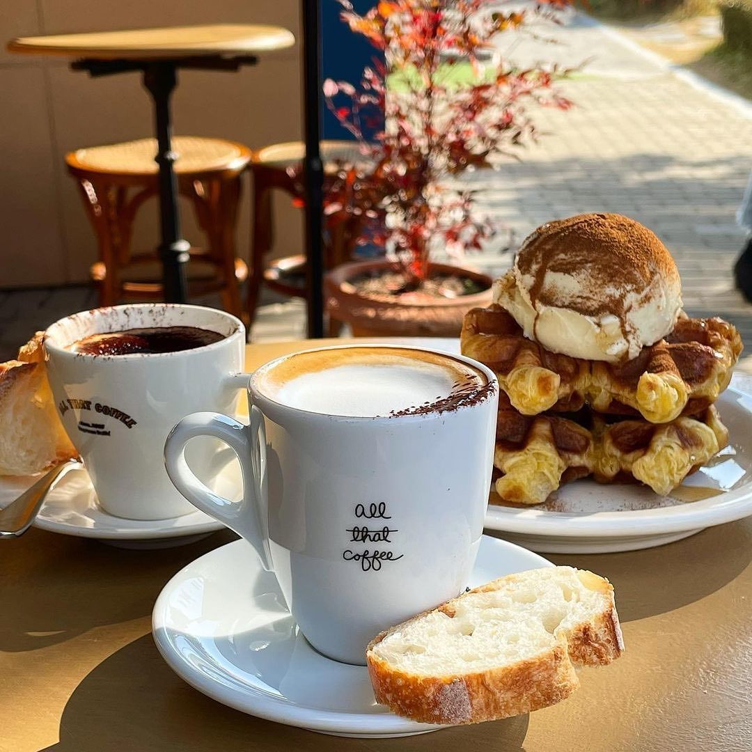 Two cups of coffee with sliced bread and waffles topped with ice cream on a cafe table
