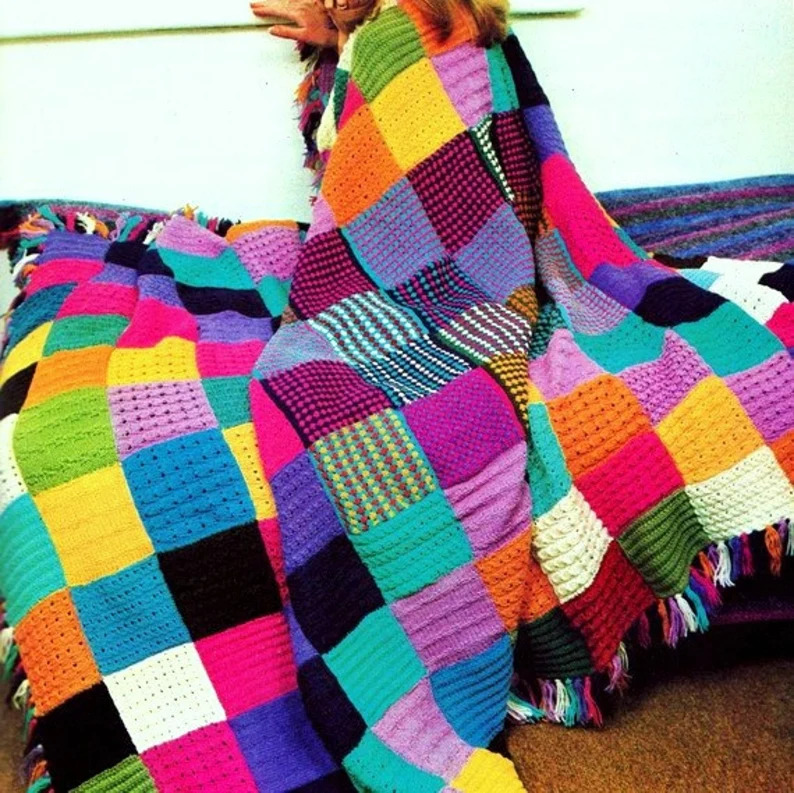 Colorful knitted patchwork blanket with multicolored squares and fringe draped over couch